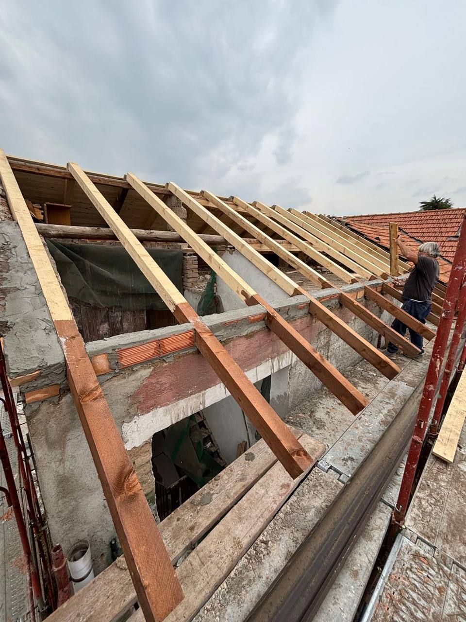 Il nostro cantiere: le travi in legno del tetto nuovo appoggiate sui muri, con uno di noi al lavoro sul ponteggio